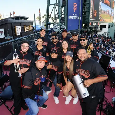 Laura Bravo's band in Gigantes jerseys with trumpets and percussion, on the stage at Oracle Park